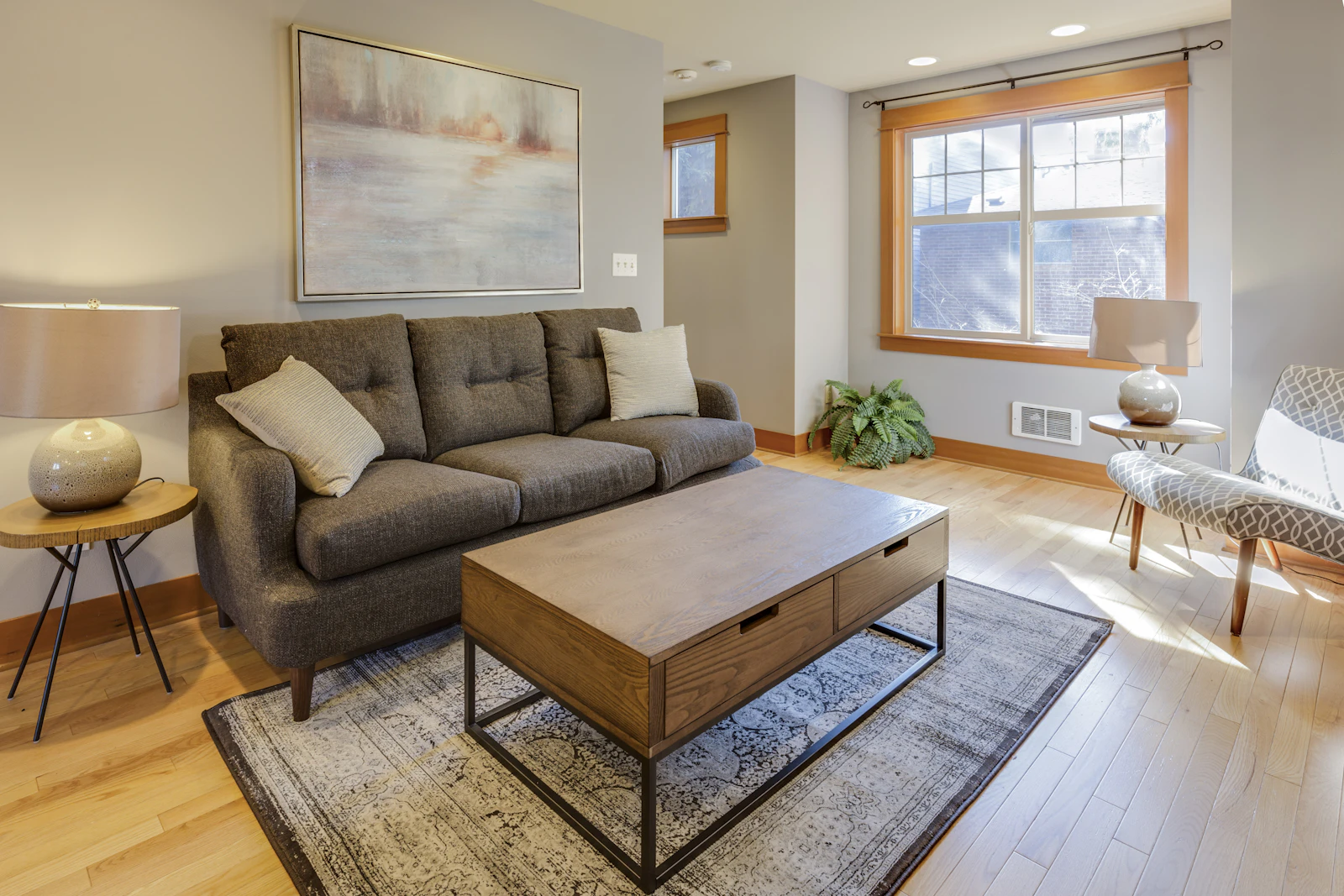 Grey sofa with a wooden coffee table and a rug in a living room with bright windows