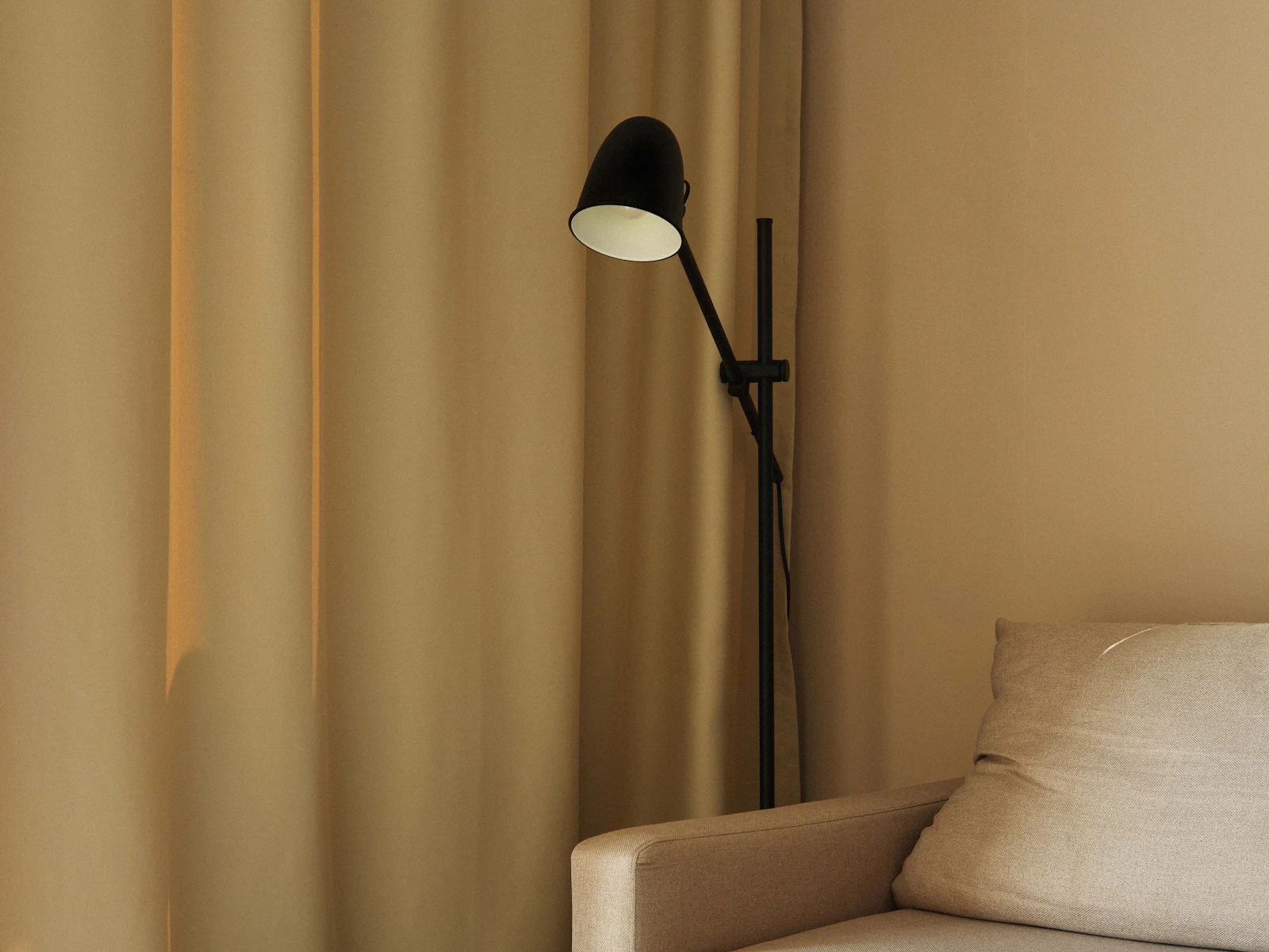 Warm beige corner with a black floor lamp and a linen cushion