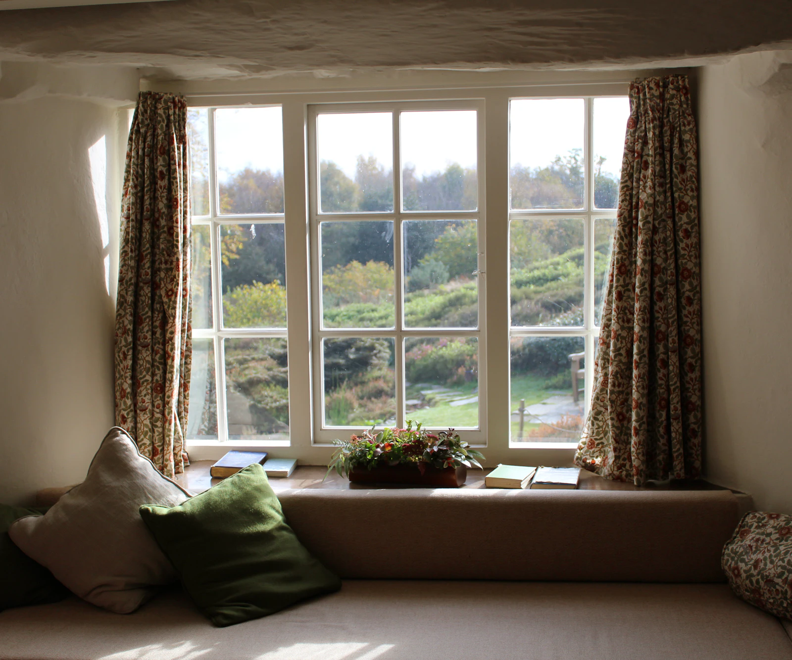 Window seat with patterned curtains drawn open to a garden view