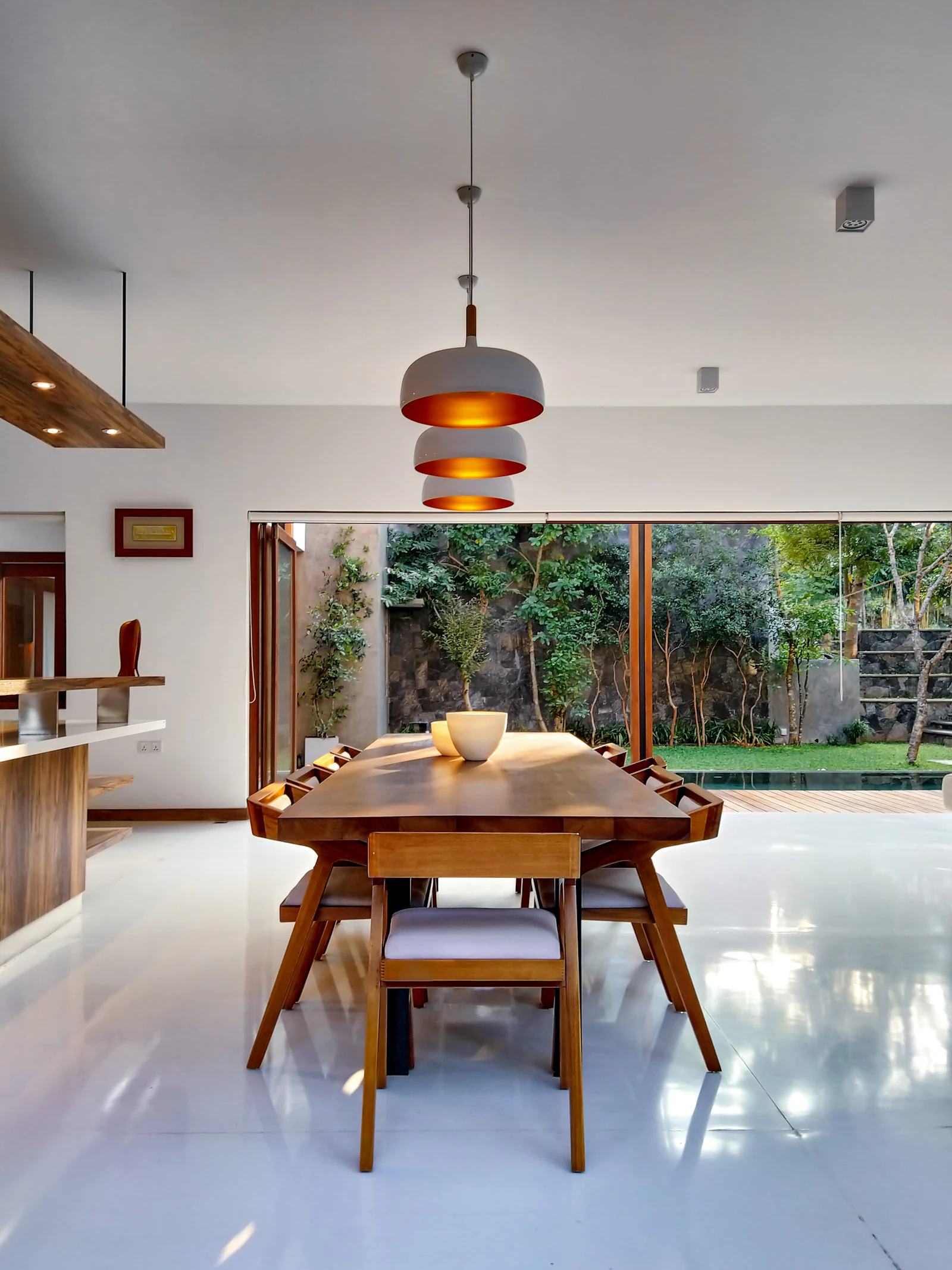 Dining table under copper pendant lights opening onto a garden