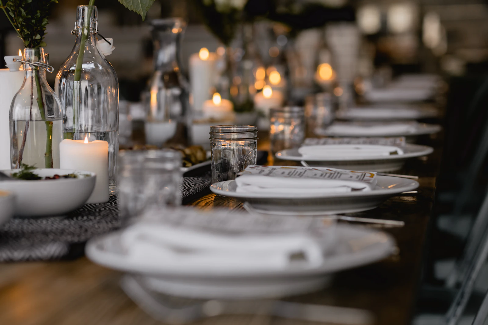 Long dining table laid with white plates, wine glasses and lit candles