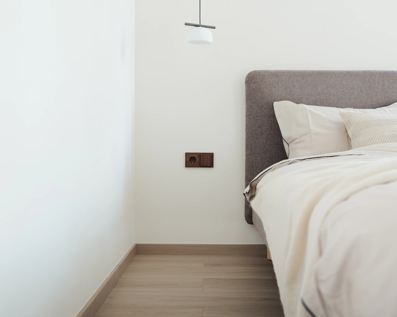 Minimal bedroom with cream bedding, a grey upholstered headboard and white walls