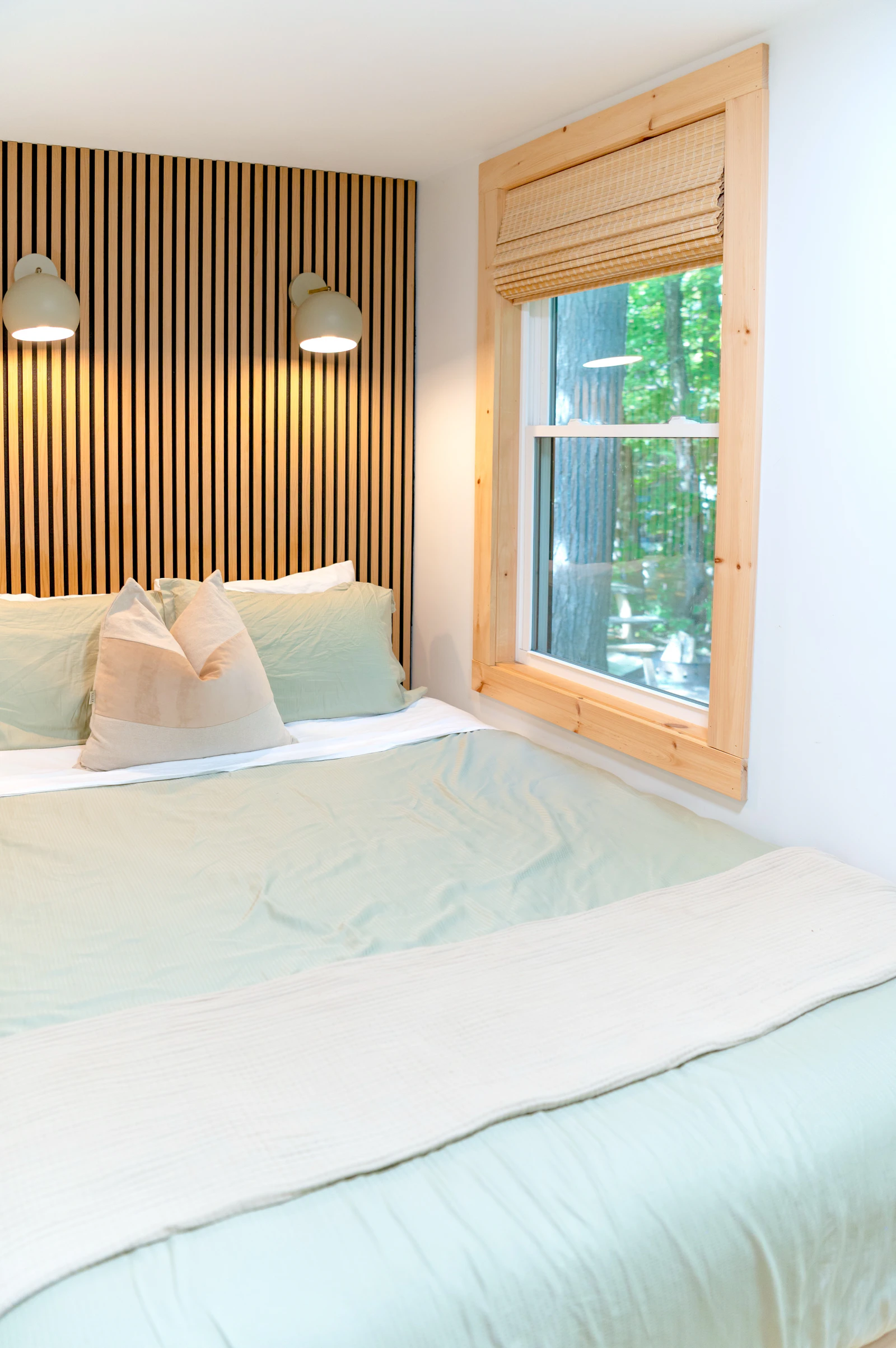 Bed with sage-green bedding against a slatted wooden wall