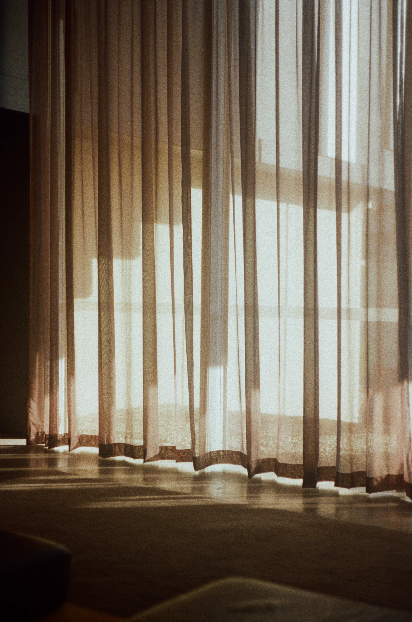 Sheer white curtains filtering warm sunlight into a bedroom