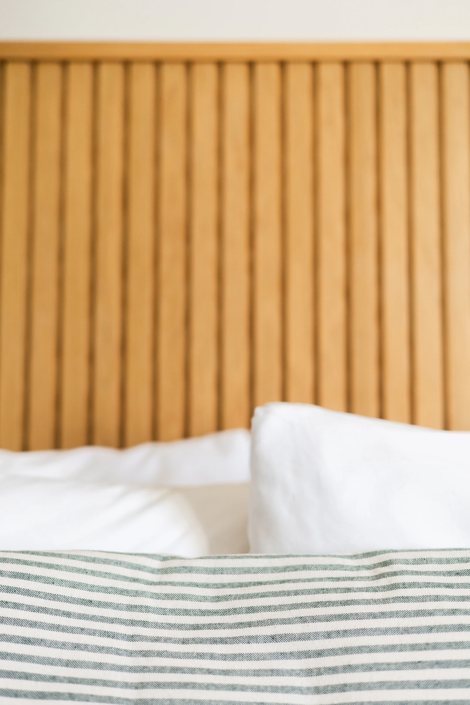 White pillows and a striped blanket in front of a slatted wooden headboard