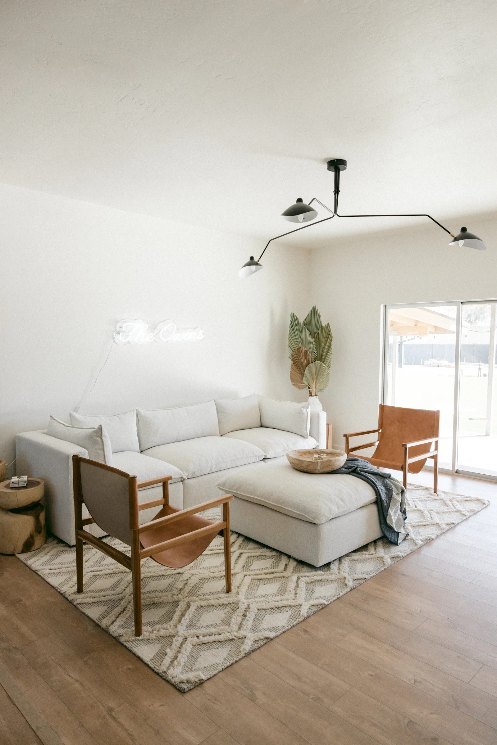 Bright living room with a white sectional sofa, leather armchairs and a sculptural ceiling light