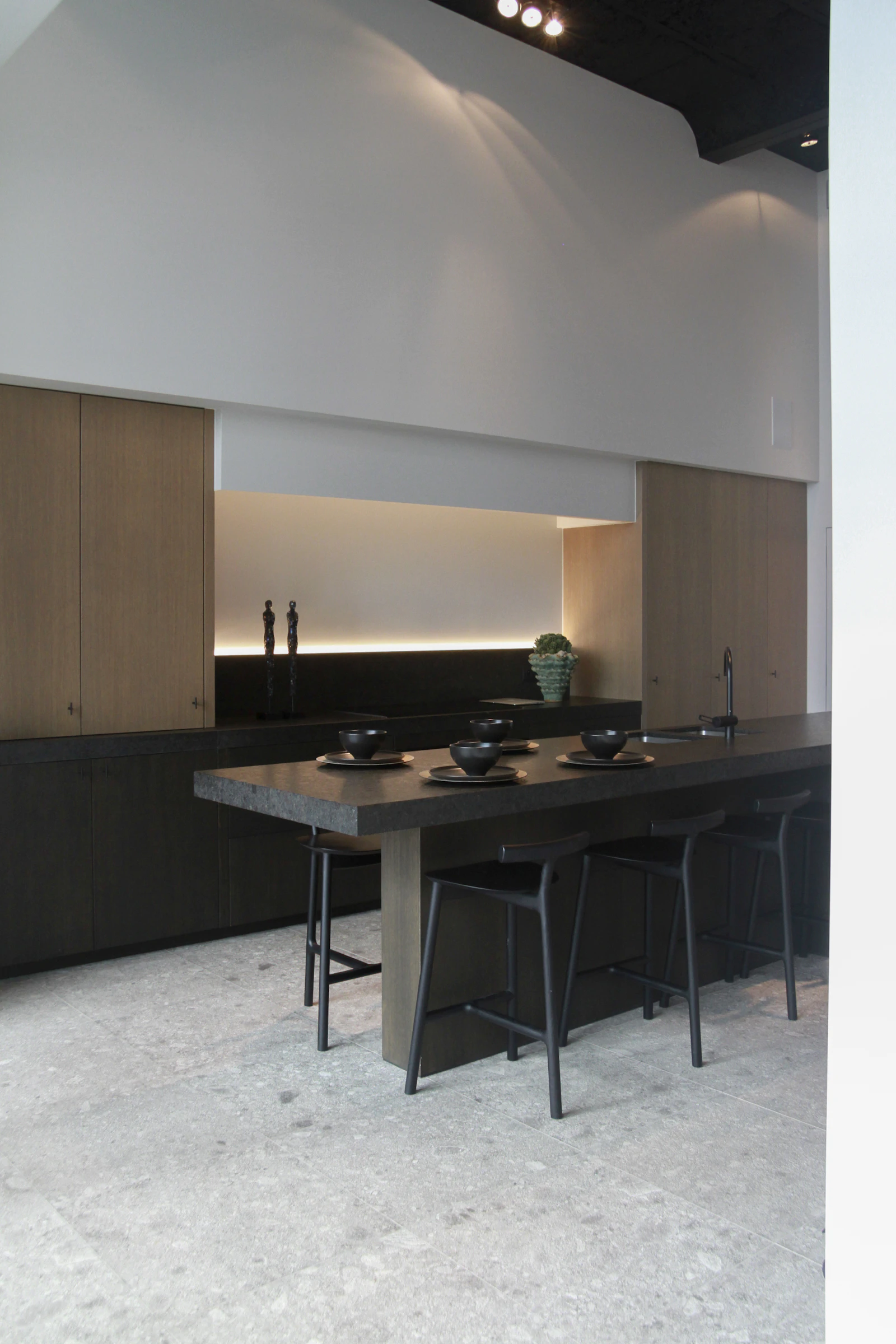Kitchen with tall oak cabinets, a long dark stone island with black stools and a softly lit recess